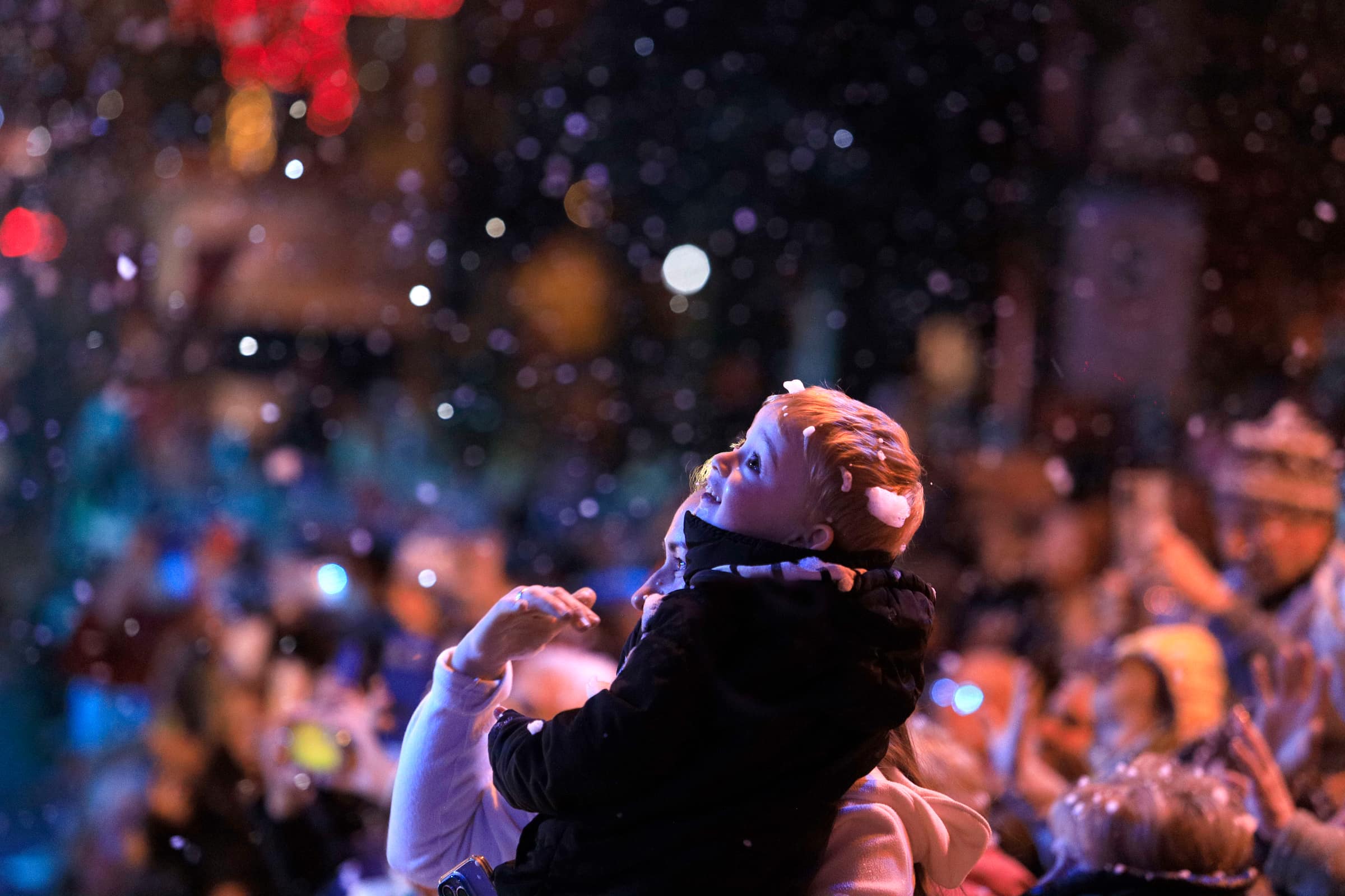 Criança no colo do pai olhando a neve cair no Natal Luz de Gramado